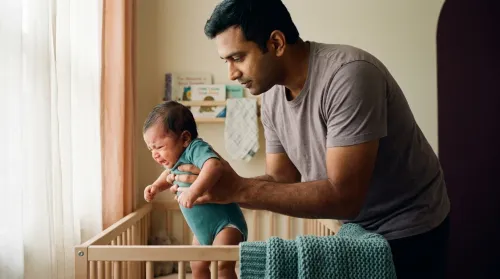 Father gently soothing his crying baby in the nursery, an everyday moment of responsive parenting in soft daylight