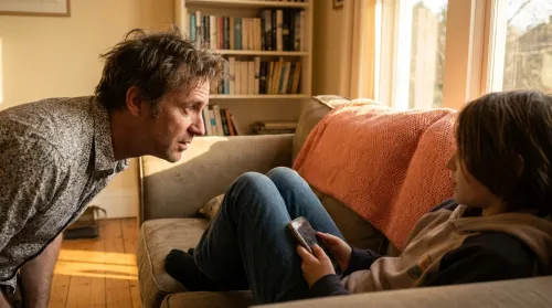 Parent and tween in conversation on a living-room sofa with a phone visible between them, raising digital citizens at home