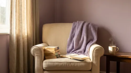 Armchair reading nook with stacked paperbacks of mothers in literature and an open novel face-down in afternoon window light